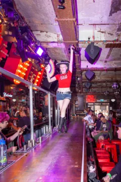 Performer che balla sul bancone al Coyote Ugly Saloon di Camden Town, Londra, con cappello da cowboy e ventaglio.