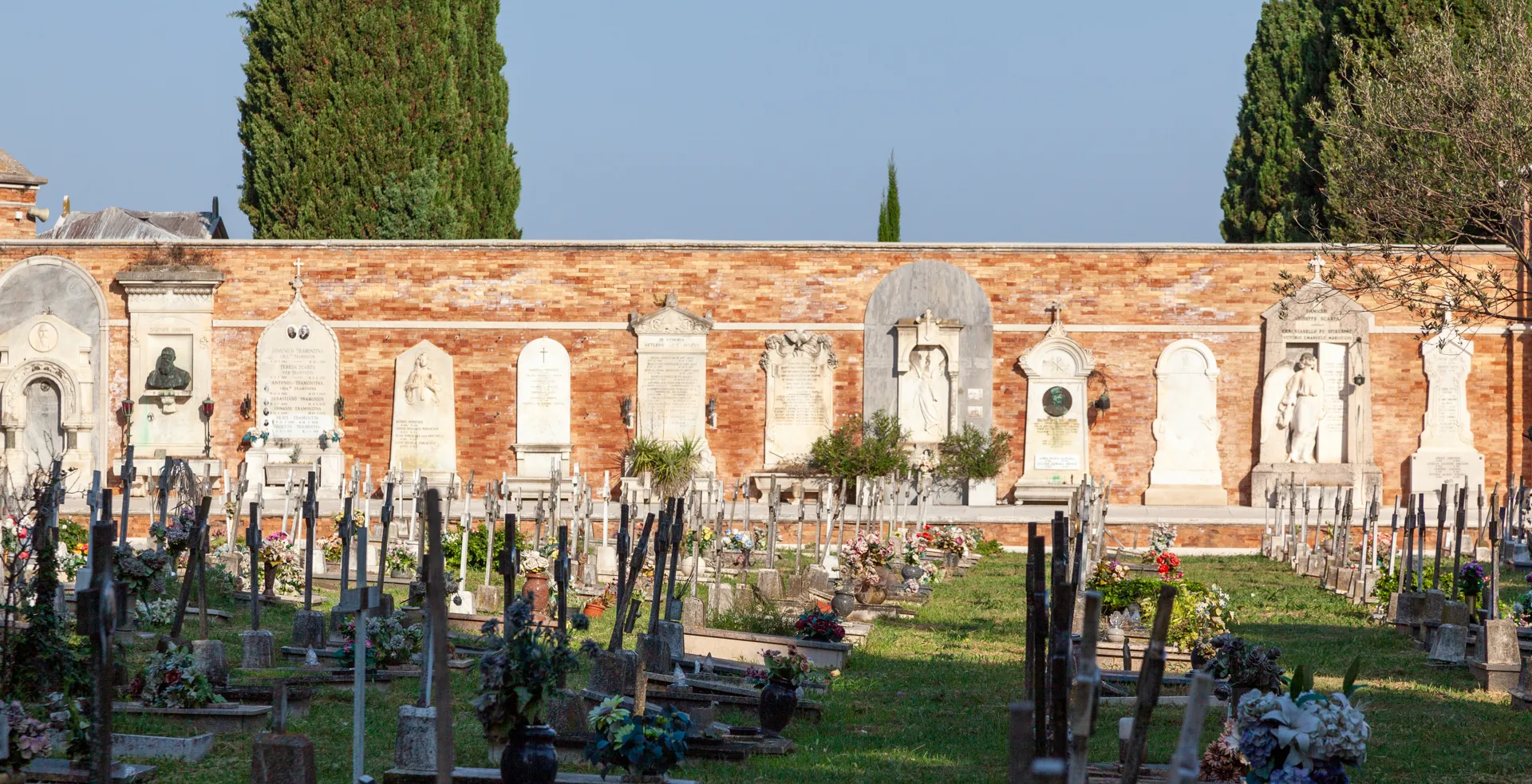Lapidi lungo il muro del cimitero di San Michele a Venezia, con rigogliosa vegetazione.