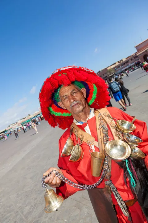 Venditore d'acqua tradizionale marocchino con abiti colorati e campanelli nella piazza Jemaa el-Fna di Marrakech, Marocco.
