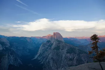 Veduta panoramica dell'Half Dome al tramonto nel Parco Nazionale di Yosemite, con il cielo limpido e le montagne circostanti illuminate dalla luce del sole calante.