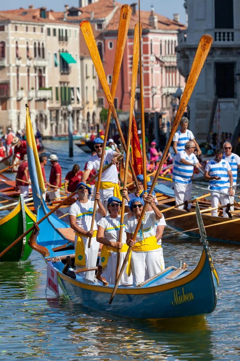 Gruppo di rematori alla Regata Storica di Venezia con bandiere e imbarcazioni decorate.