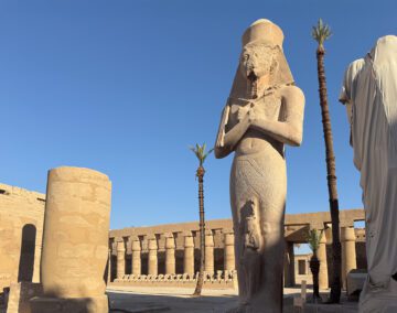 Statua colossale di faraone nel Tempio di Karnak a Luxor, con rilievi e colonne sullo sfondo