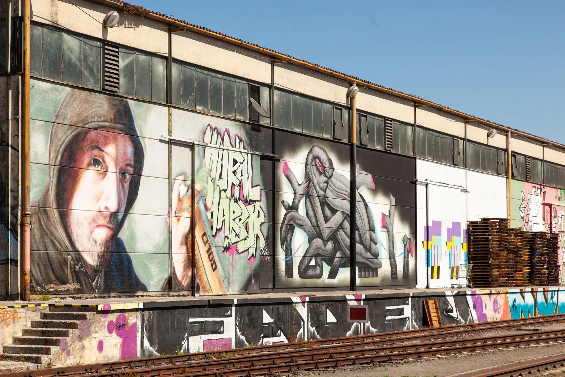 Murales con personaggi surreali e colori vivaci in un'area industriale di Linz.