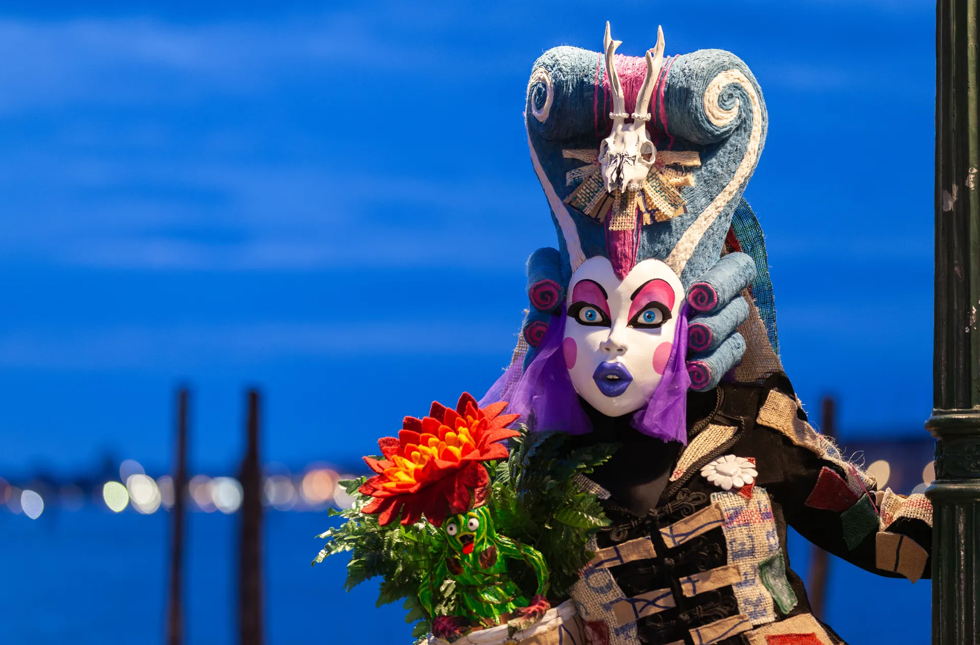 Maschera fantasy con colori vivaci e copricapo elaborato davanti alla laguna veneziana all'alba.