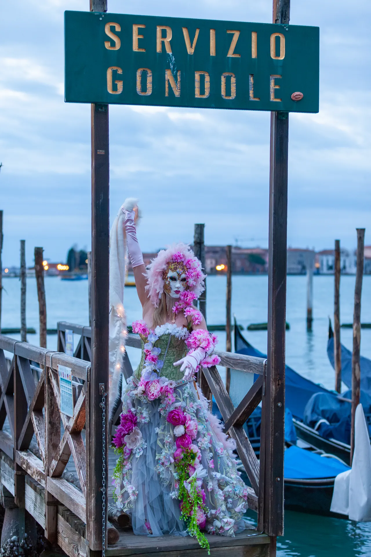 Maschera floreale con decorazioni romantiche sotto il cartello 'Servizio Gondole' a Venezia.
