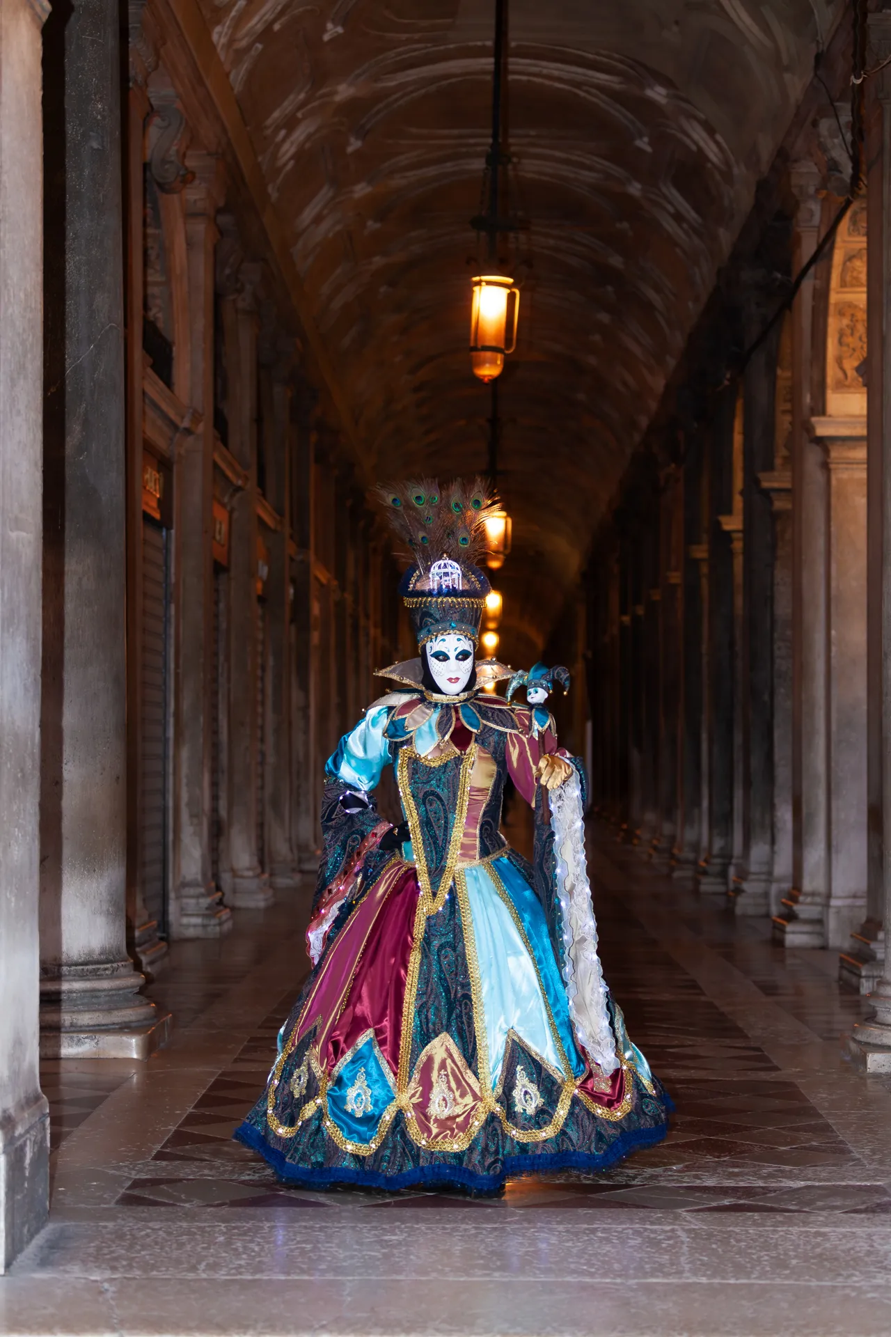 Maschera veneziana in costume elaborato sotto i portici delle Procuratie Nuove a Venezia durante il Carnevale.