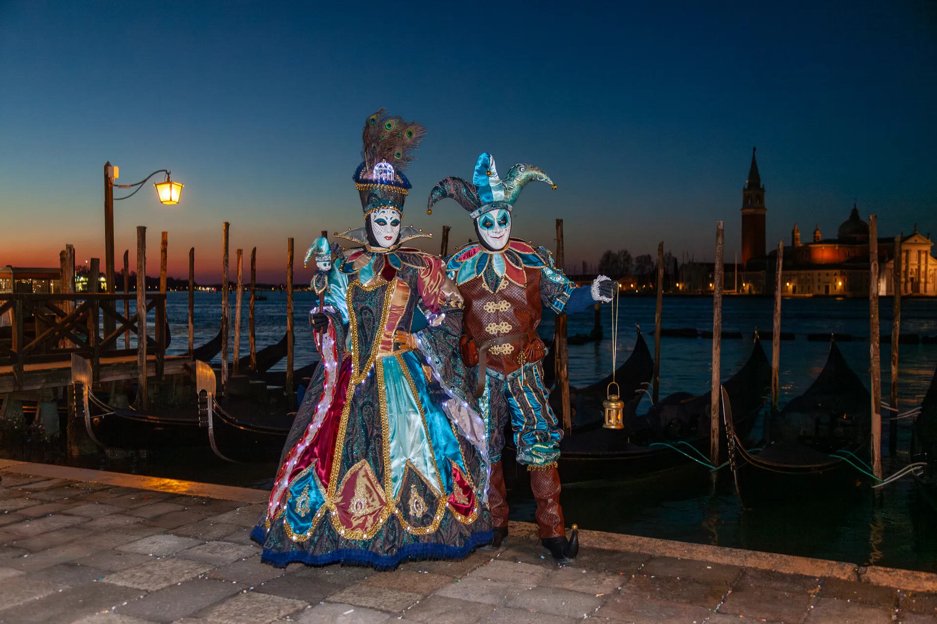 Coppia in maschera con abiti blu e oro e gondole sullo sfondo al Carnevale di Venezia.