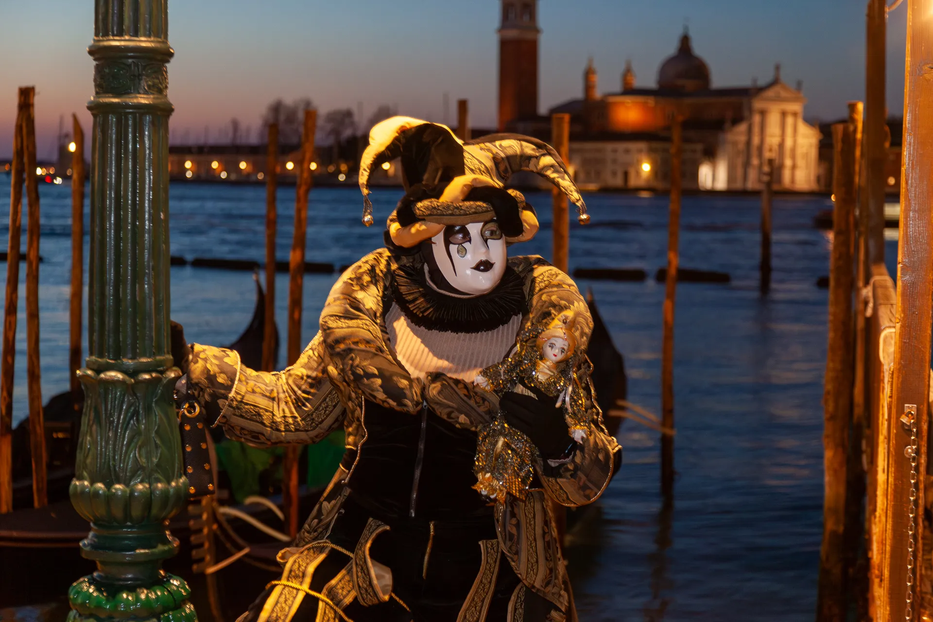 Pierrot malinconico con bambola in mano e gondole veneziane sullo sfondo.
