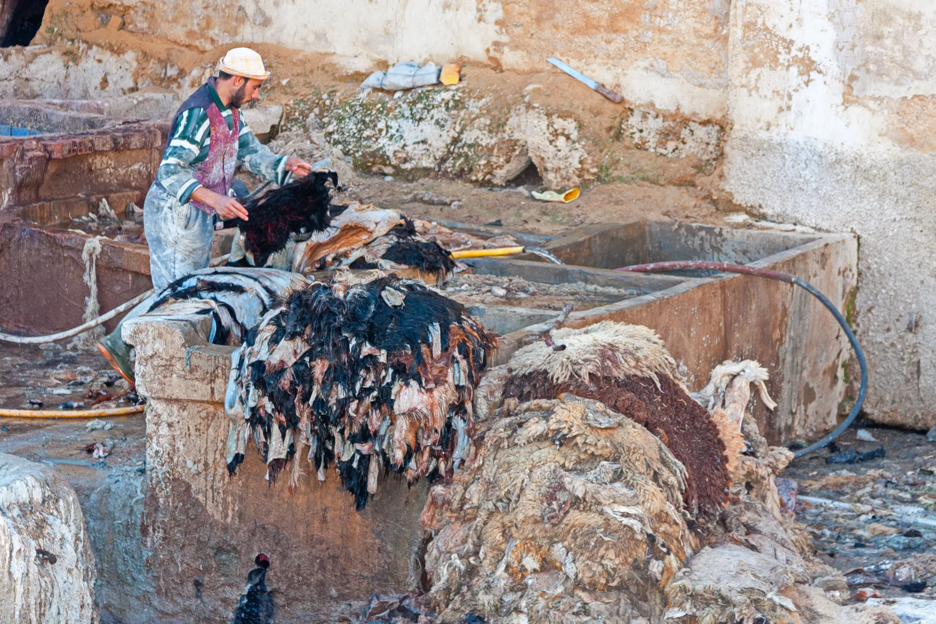 Operaio al lavoro in una conceria tradizionale di Fès, immerso nella lavorazione delle pelli grezze tra vasche in pietra e strumenti artigianali.