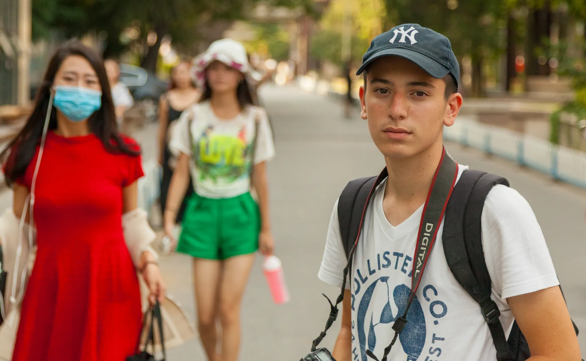 Giovane con cappellino NY e macchina fotografica a tracolla
