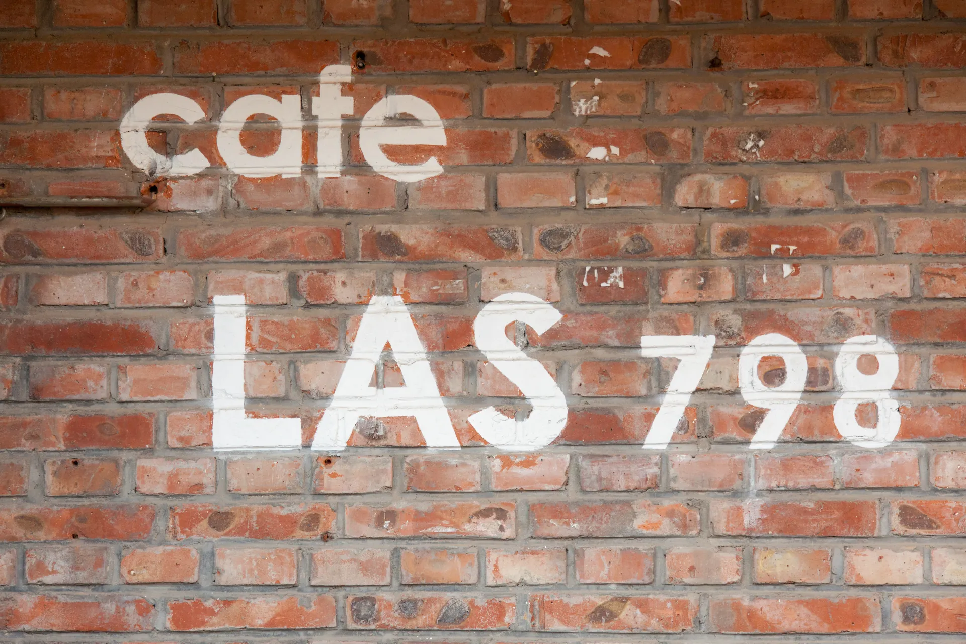 Scritta bianca 'cafe LAS 798' su muro di mattoni rossi