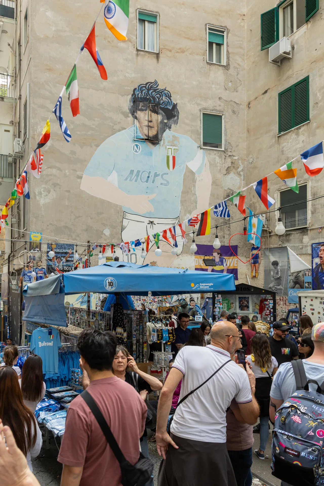 Grande murale di Maradona circondato da bandiere e persone