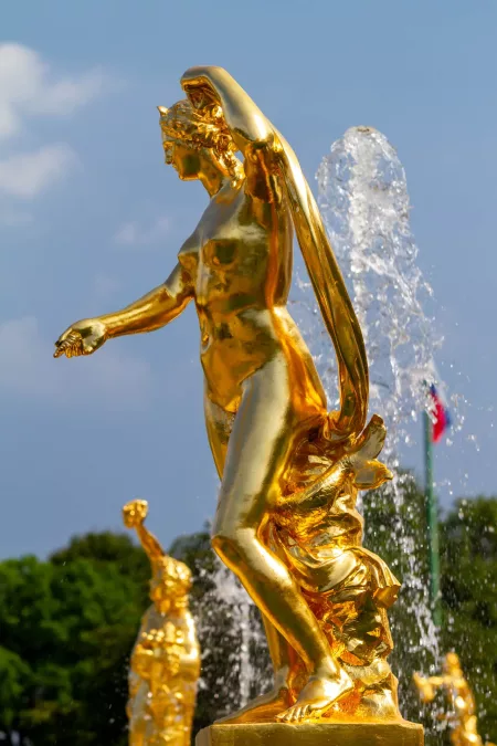 Statua dorata di una figura femminile nella fontana di Peterhof, San Pietroburgo, con getti d'acqua che creano un contrasto elegante con il cielo blu.